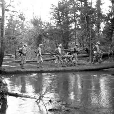 Soldiers crossing a stream on a fallen tree