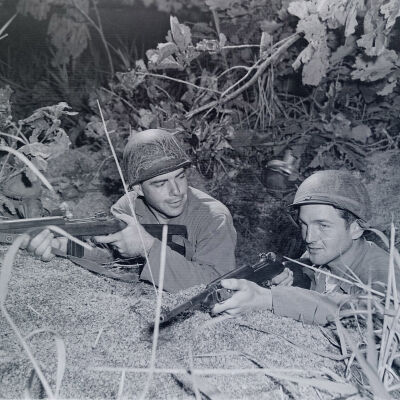 Two soldiers posed behind a rock in foxhole with their weapons