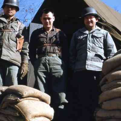 Soldiers standing outside of a tent surrounded by sandbags