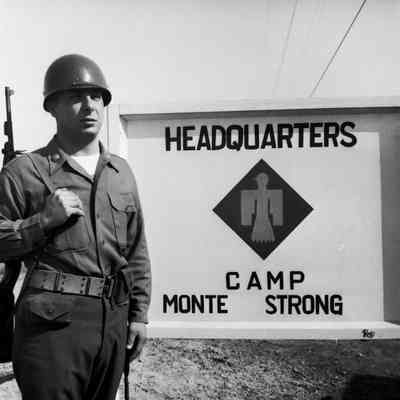 Soldier standing guard in front of sign "HQ Camp Monte Strong"