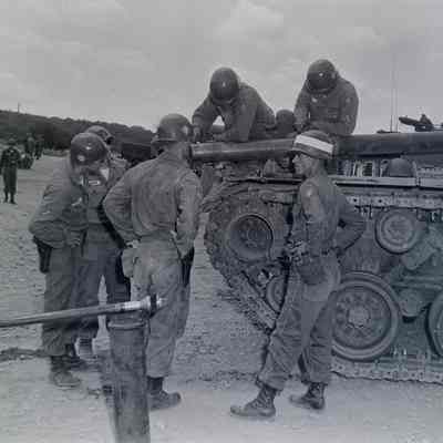 Group of soldiers gathered around the front of a tank on practice range