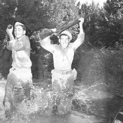 Soldiers running across a stream with rifles