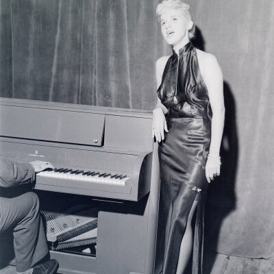 Woman entertainer singing next to a piano