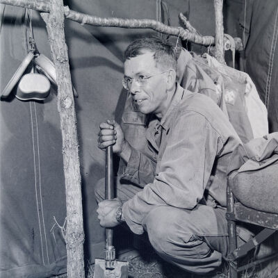 Soldier using entrenching tool to build a rough rack inside a tent