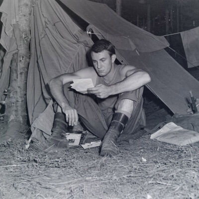 Soldier in front of pup tent reading letter