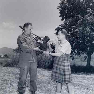 Scotsman teaching soldier how to play bagpipes