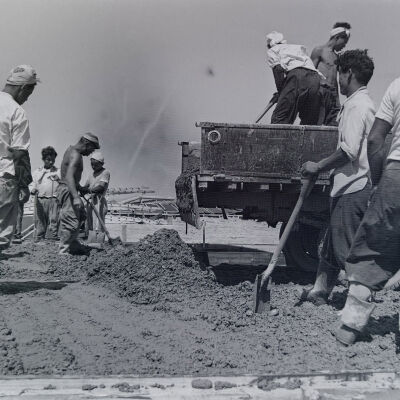Civilian construction crew pouring concrete and leveling floor for Quonset hut