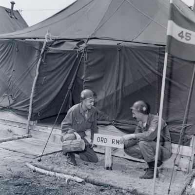Two soldiers posting and "Orderly Room" sign outside a tent