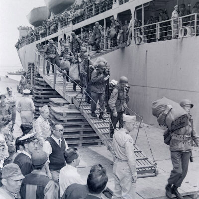 Soldiers with weapons and field gear off-loading from troop ship