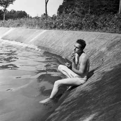 Soldier shaving while sitting at the edge of a lake