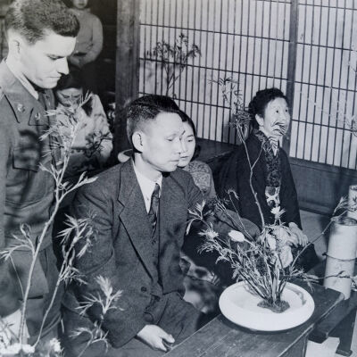 Soldier and Japanese civilians examining potted plants
