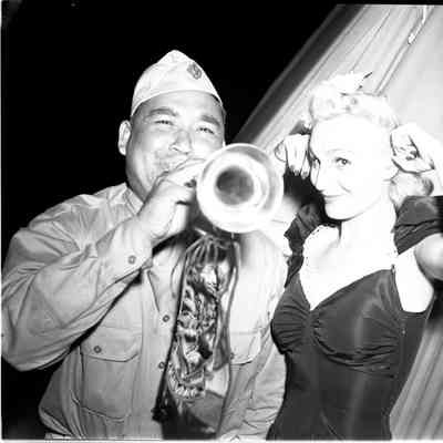Soldier playing a bugle while a female entertainer stands beside him