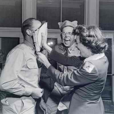 A female Army Service Club member shoves a pie in the face of a soldier during a party