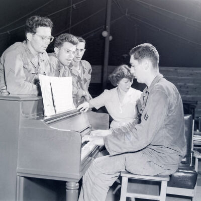 Soldiers and Army Service Corps lady singing around a piano
