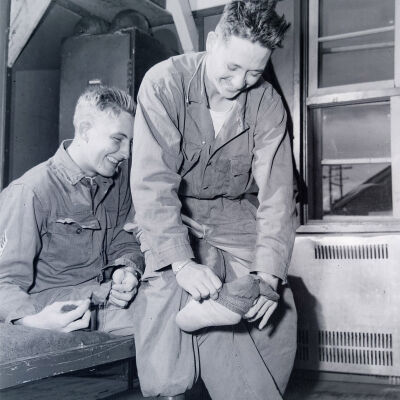 Soldier sitting on bunk having his socks put on by another soldier