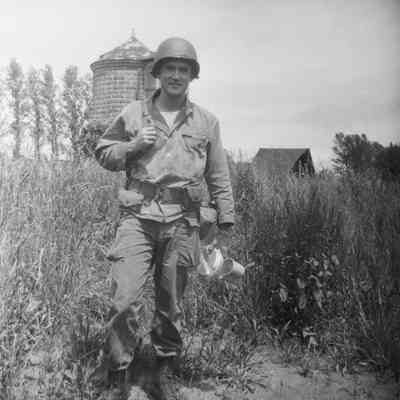 Soldier holding his mess gear with a silo and barn in the background