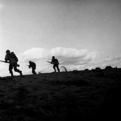 Soldiers running across beach with rifles