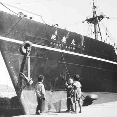Boys on pier looking at cargo ship Enkei Maru