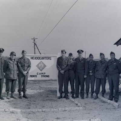 Group of soldiers in front of a sign for Camp Monte Strong