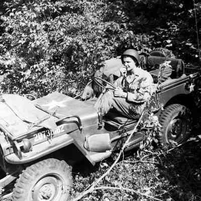 Soldier using the radio in a jeep while moving through a wooded area