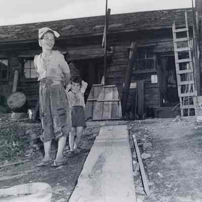 Mother and child in ragged clothing in front of a makeshift dwelling