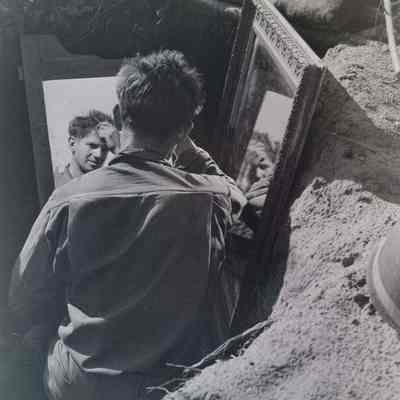 Soldier combing hair with mirror in dugout