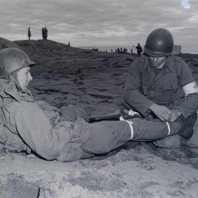 Medic splinting a soldier's leg on a beach