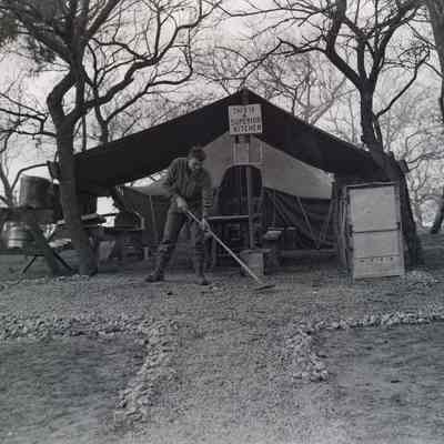 Soldier rakes rocks and gravel in front of field kitchen
