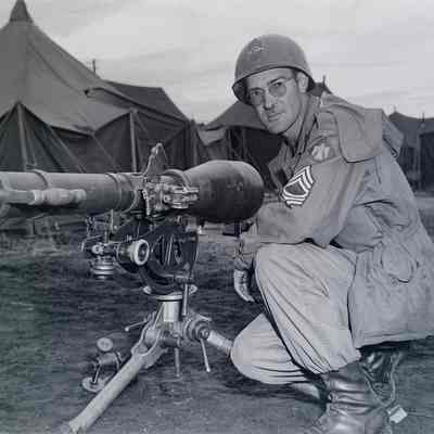 Soldier examining a recoilless rifle with tent camp in background