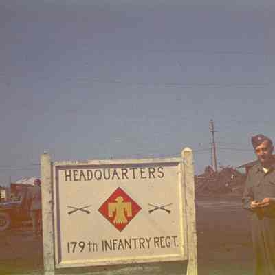 Soldier standing in front of a sign for the Headquarters of the 179th Infantry