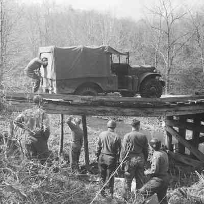 Soldiers fixing a truck that broke through a wooden bridge