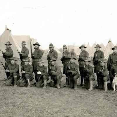 Soldiers posing with rifles in front of tents