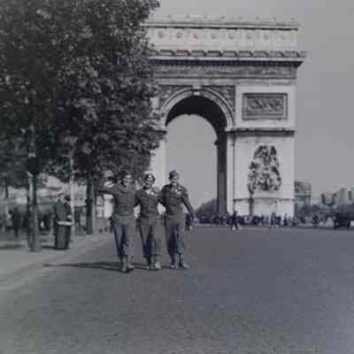 Three soldiers posing for a group shot in front of the Arc de Triomphe