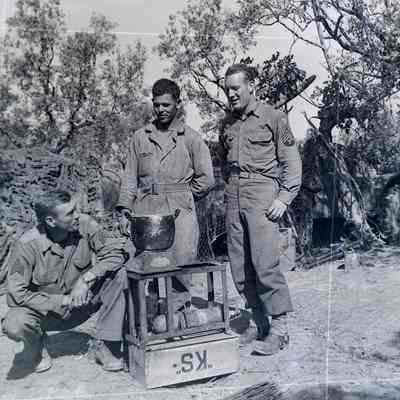 Soldiers standing around improvised camp stove