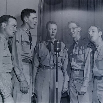 Five soldiers singing around a microphone