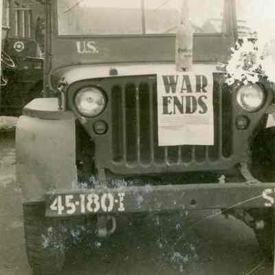 Hood of a jeep adorned with a bottle of alcohol and a "War Ends" newspaper