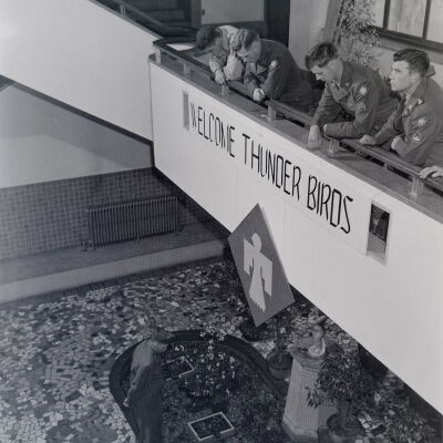 Soldiers on a balcony hung with a "Welcome Thunder Birds" banner