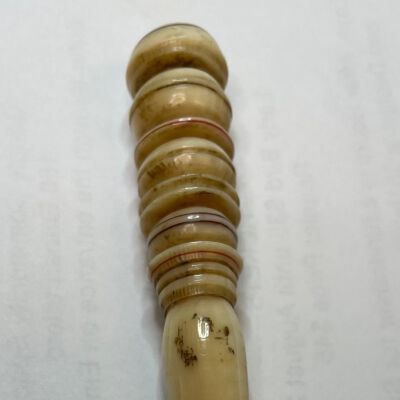 #5: A bone stiletto with circular carvings increasing in size to the top with a pointed awl at the opposite end. There are deep channels between the circular carvings and some of them are embellished with either red or black lines.