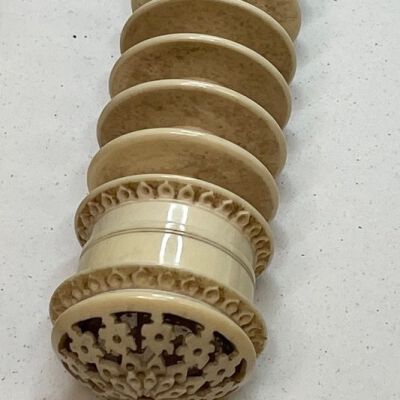 #5: Carved bone bar with seven carved discs dividing the center staff creating sections for winding thread. The top has a finial, and the bottom with a carved floral design