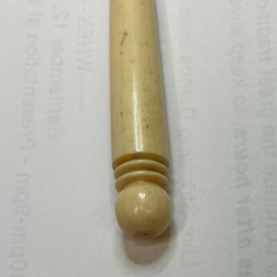 #2: A bone stiletto with a narrow pointed tip, the round instrument getting wider towards the top where there is a carved  ball shape with two saturn-type rings beneath it