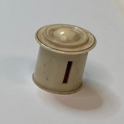 #6: A bone tape measure barrel with a carved top. There is a slit on the side of the barrel to pull out the tape