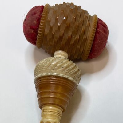 #5: A long carved bone case housing a crochet hook with a Tagua nut bulb-shape forming at the top, which is topped with a barber-pole carved bone bulb. Above this bulb is a horizontal Tagua nut carved barrel with red velvet pincushions at each side.