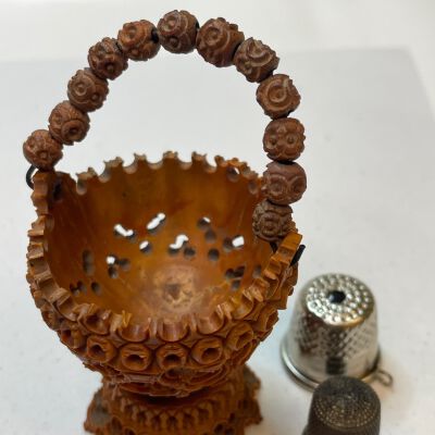 #3: Carved nut thimble basket with a handle of carved roses and perforated circles along the side of the basket. All on top of a carved base with two later thimbles