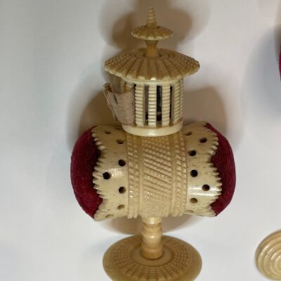 #4: The bone carved pedestal with horizontal red velvet pincushions flanking the sides and a cap with a taupe hand-lettered tape measure, the total resembling a pagoda.