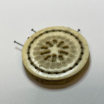 #3: Carved (Bone or ivory) pin keep shaped as a circle with carved cut outs with green silk showing through. Sandwiched between the hard surface is soft layer of wool covered in green silk. Pins are inserted parallel to the hard surface into the silk.