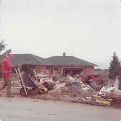 Man dumping blue wheelbarrow into pile of debris
