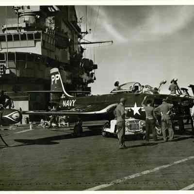 An F9F Panther refuels on the flightdeck. Behind the refueling panther the aircrew of the Yorktown can be seen defacing a panther from a different carrier. Pilots who accidently landed on the wrong carrier often found themselves having to endure the pranks of that carrier's crewmen.