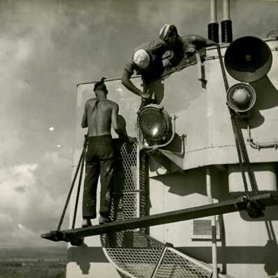2019.06.48-3: 3 sailors standing outside doing work on one of Laffey's 40 mm gun mounts.