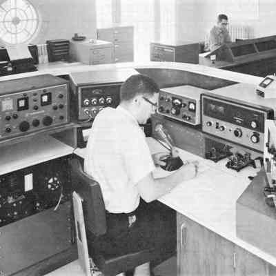 W1AW Maxim Memorial Station, cr. 1965. Equipment in use (on desk, from left): Hammarlund HQ-150 reciever, Hallicrafters HT-32B transmitter, Collins 75S-1 receiver, Hallicrafters HT-33B linear amplifier, and unknown piece at right. Background: Sloping console with Collins S/Line, and an unused Hammarlund HX-500 transmitter (on the operator's right).: Image: From ARRL publication "Operating an Amateur Radio Station," copyright 1965