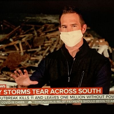 "TV reporter delivering the news with a mask on"